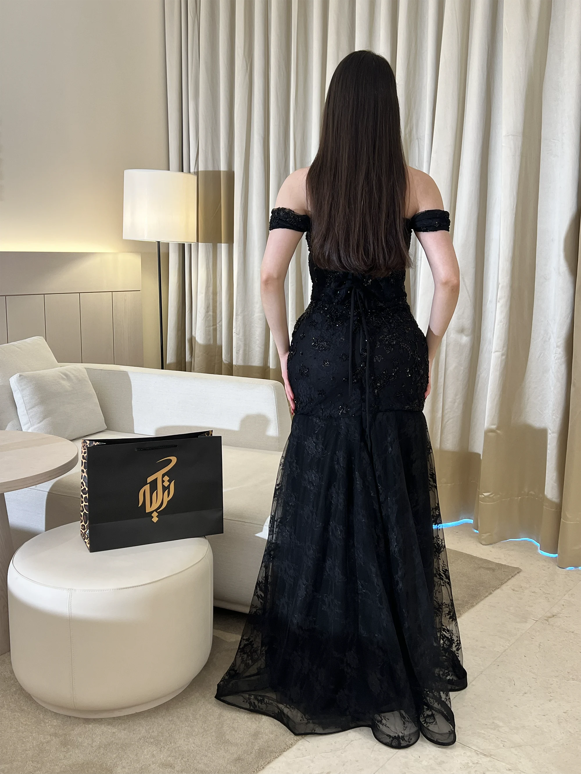 إطلالة خلفية كاملة تبرز قصة حورية البحر الانسيابية وتفاصيل الظهر المزود برباط أنيق (Corset back)، مع امتداد قماش الدانتيل الأسود الفاخر على الأرض.