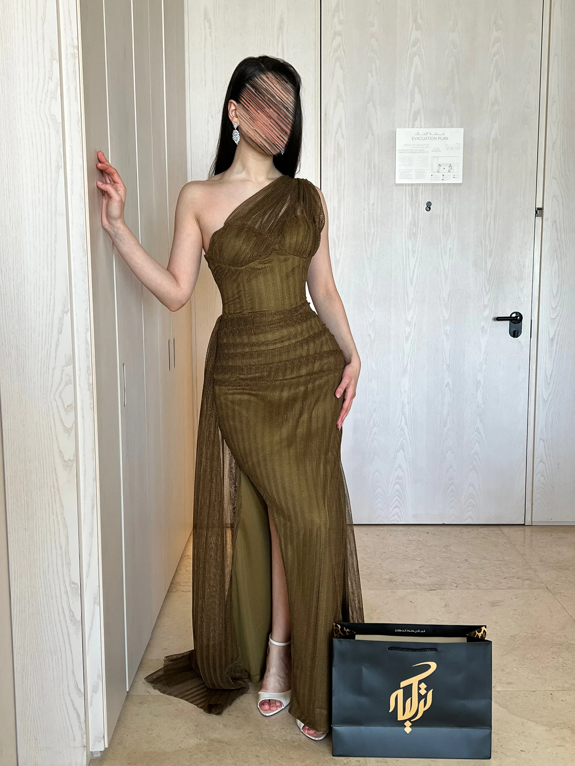 تبرز فخامة اللون الزيتي بقماش الجوبير، مع قصة ماسكة (Slim Fit) تحدد القوام، وتصميم الكتف الواحد الجذاب مع فتحة ساق جانبية تفيض بالأنوثة الراقية.