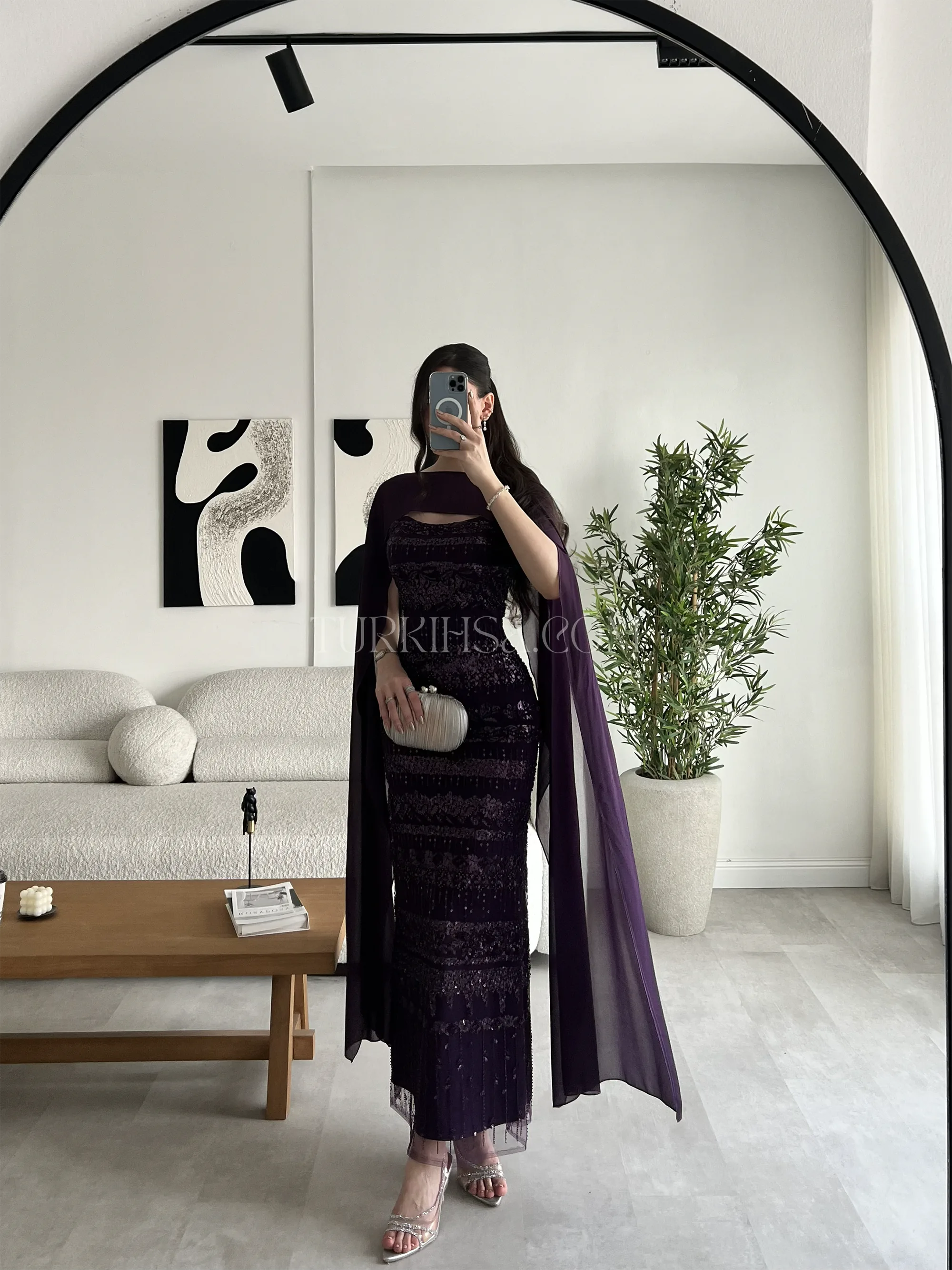 وضعية وقوف بزاوية جانبية توضح انسيابية قصة الكايب من الخلف وكيف يغطي الأكتاف والظهر برقي تام، ويضيف طولاً ملكياً للإطلالة.