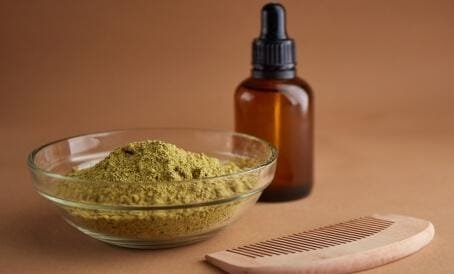 Natural henna in a glass bowl with a bottle of essential oil and a wooden comb