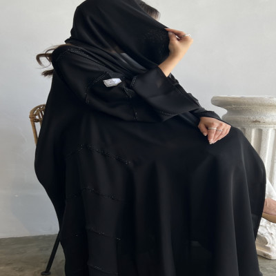 Model wearing a black kloosh abaya with elegant crystal embellishments on sleeves and edges