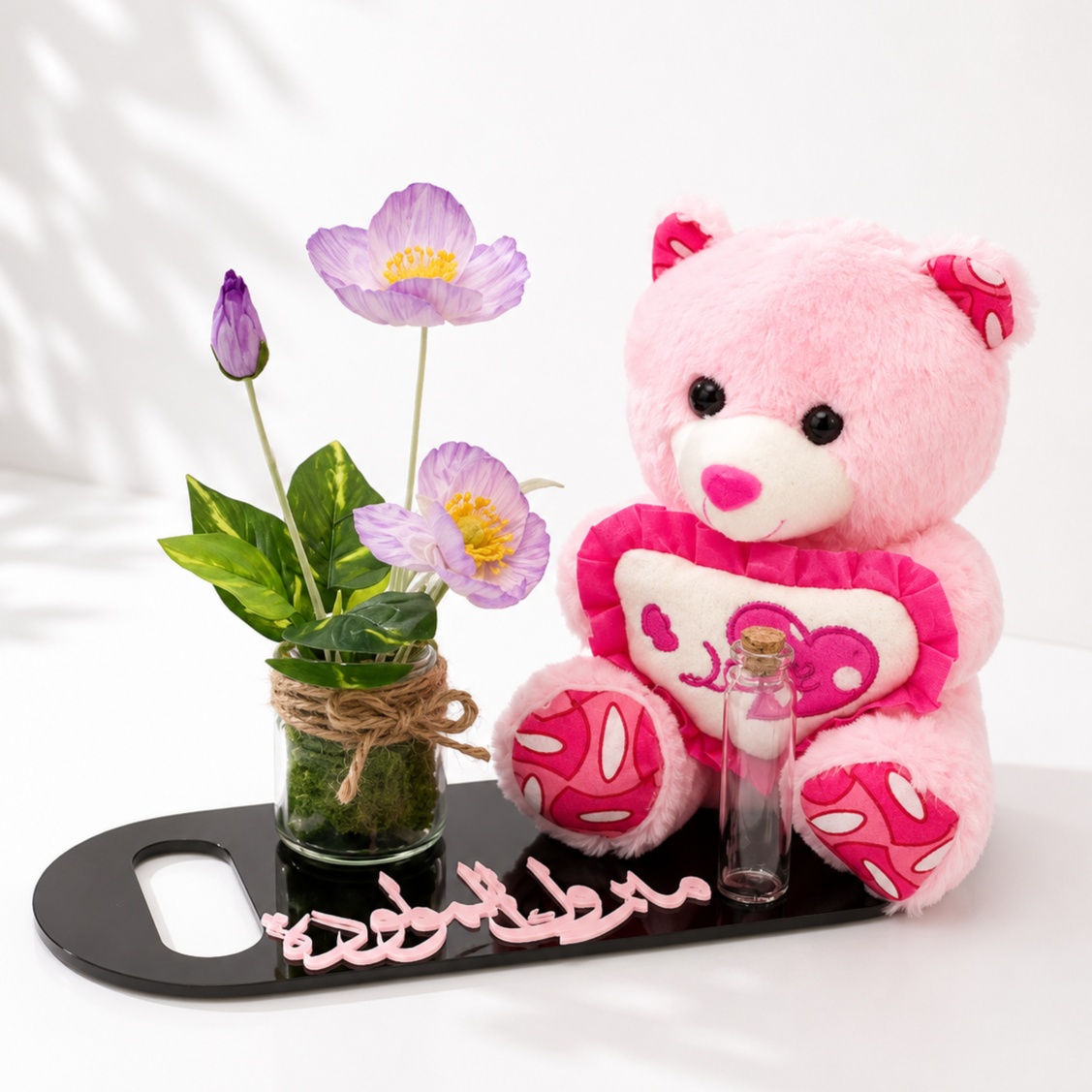 Baby girl gift set featuring a pink teddy bear, floral arrangement in a glass vase, and a decorative base with a congratulatory message.