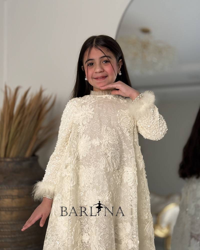 A cream-colored girl's dress with shimmering decorative details.