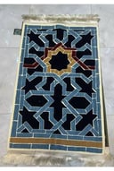 سجادة صلاة أنيقة بتصميم هندسي إسلامي مميز باللونين الأزرق والأسود، مع إطار ذهبي وتفاصيل باللون الأحمر الداكن.