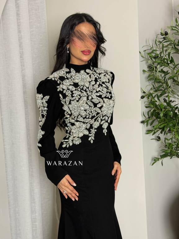 فستان سهرة أسود محتشم بياقة عالية وتطريز كريستال فضي على الصدر والأكتاف