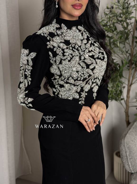 فستان سهرة أسود محتشم بياقة عالية وتطريز كريستال فضي على الصدر والأكتاف