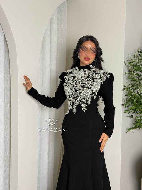 فستان سهرة أسود محتشم بياقة عالية وتطريز كريستال فضي على الصدر والأكتاف